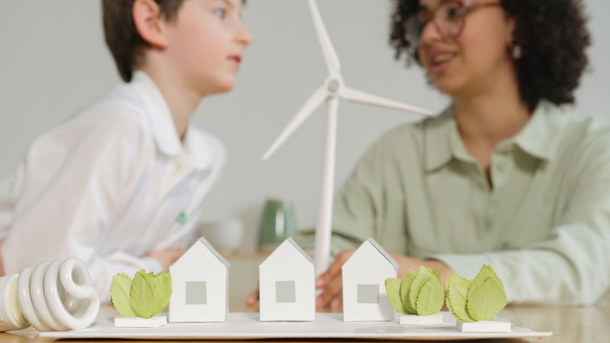 Modele energooszczędnych domów, żarówka LED i turbina wiatrowa symbolizujące świadectwo energetyczne budynku.
